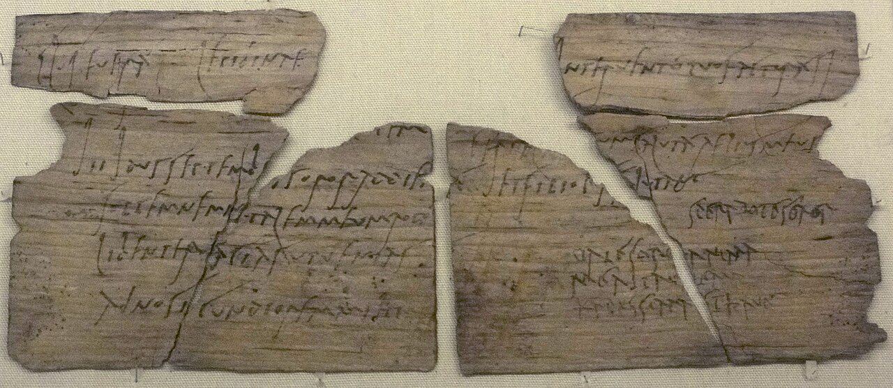 Fragments of a thin wooden writing tablet covered in Roman cursive handwriting in ink