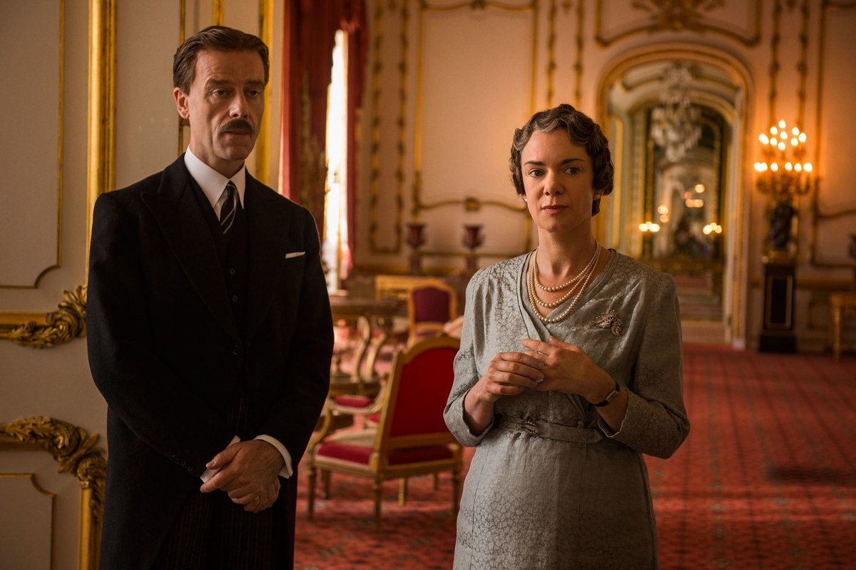 Pip Torrens as Tommy Lascelles, in a dark morning coat, standing beside Victoria Hamilton as Queen Elizabeth in a gilded palace room