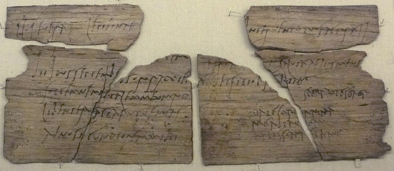 Fragments of a thin wooden writing tablet covered in Roman cursive handwriting in ink